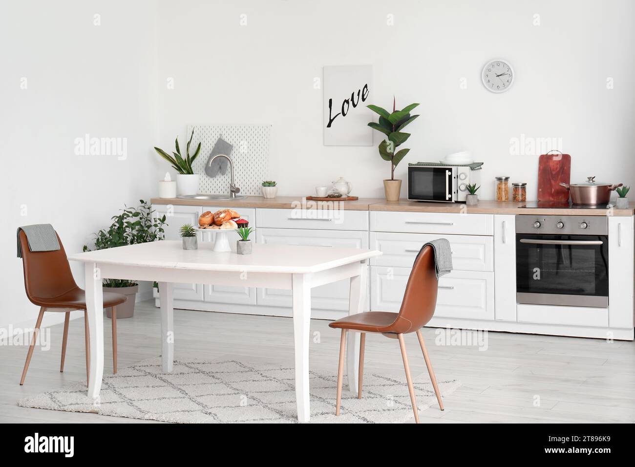 Interior of modern kitchen with pastry and houseplants on dining table ...