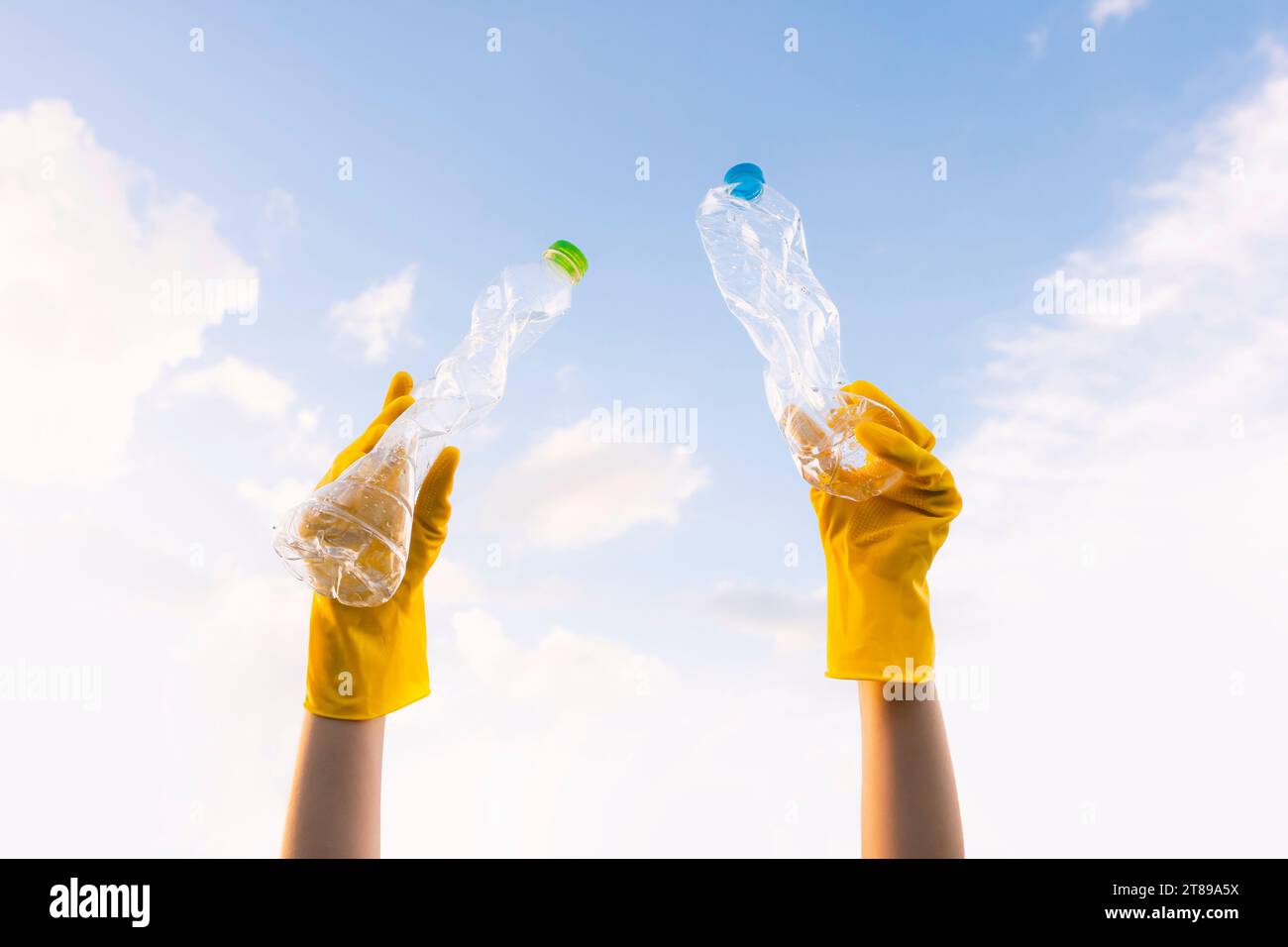 A young volunteer's hand lifts trashed plastic bottles into the sky. On World Environment Day Stock Photo