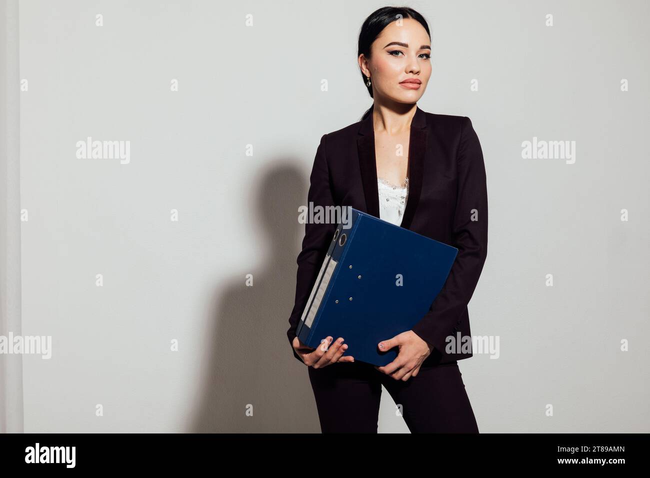 a business woman in a black suit stands with a folder in an office ...