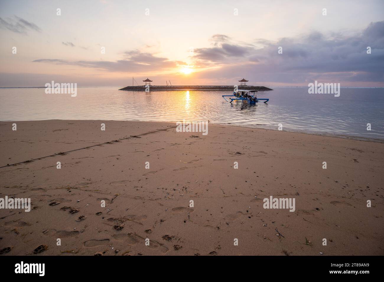 Sunrise at the sandy beach of Sanur. Temple in the water. Traditional fishing boat, Jukung on the beach. Hindu faith in Sanur on Bali. Dream island Stock Photo
