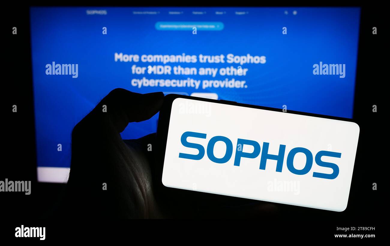 Person holding cellphone with logo of British security software company Sophos Group plc in front of business webpage. Focus on phone display. Stock Photo