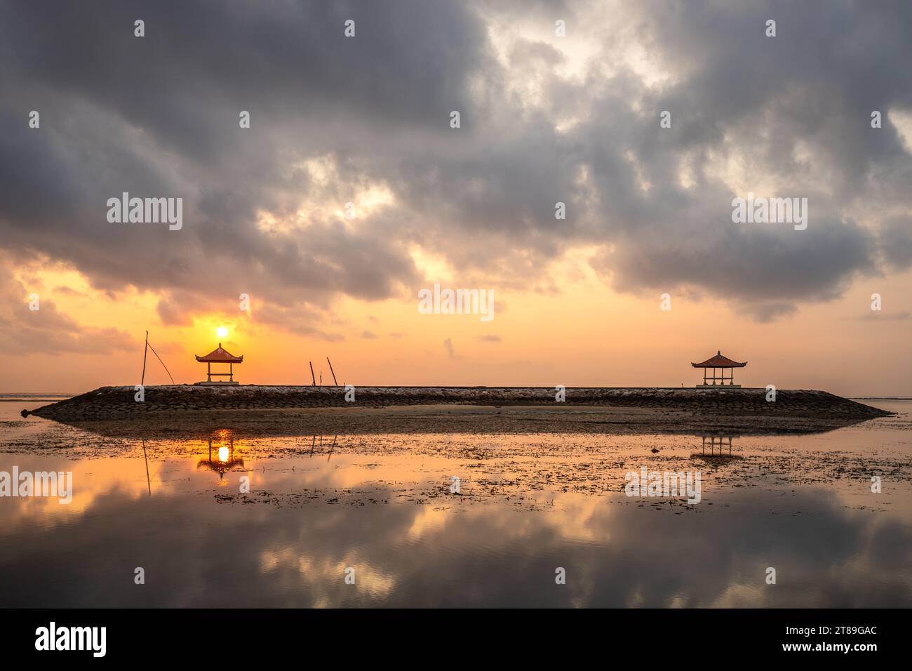 Magical sunrise with clouds in the sky. Dramatic sky at Sanur beach, Denpasar in Bali. Temple in the calm sea in the morning. Tropical landscape shot Stock Photo