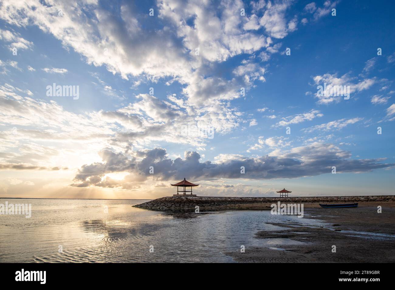 Magical sunrise with clouds in the sky. Dramatic sky at Sanur beach, Denpasar in Bali. Temple in the calm sea in the morning. Tropical landscape shot Stock Photo