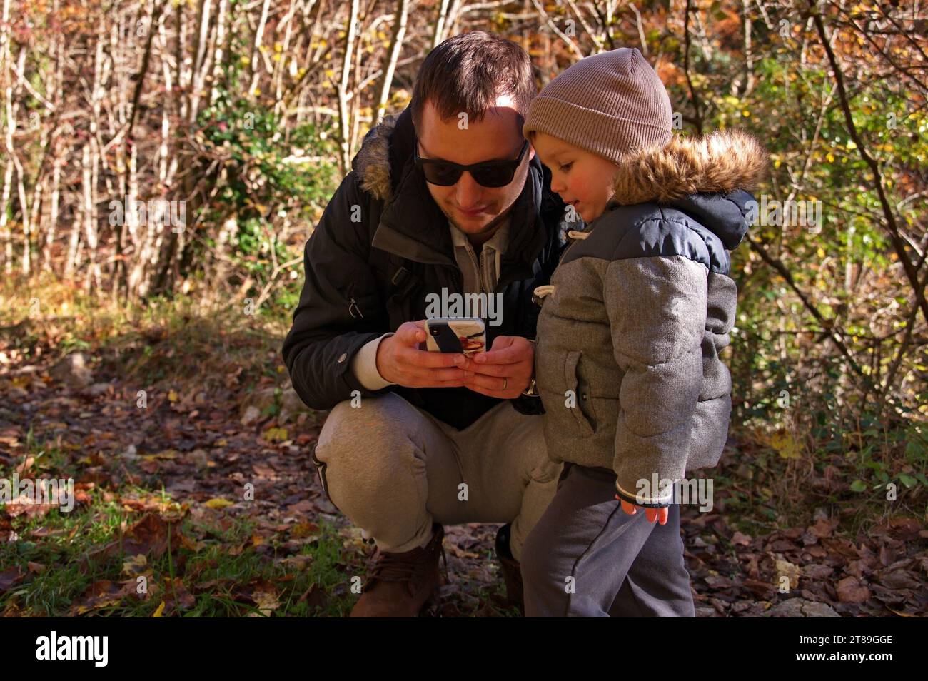 Father and his toddler using mobile phone in the forest Stock Photo