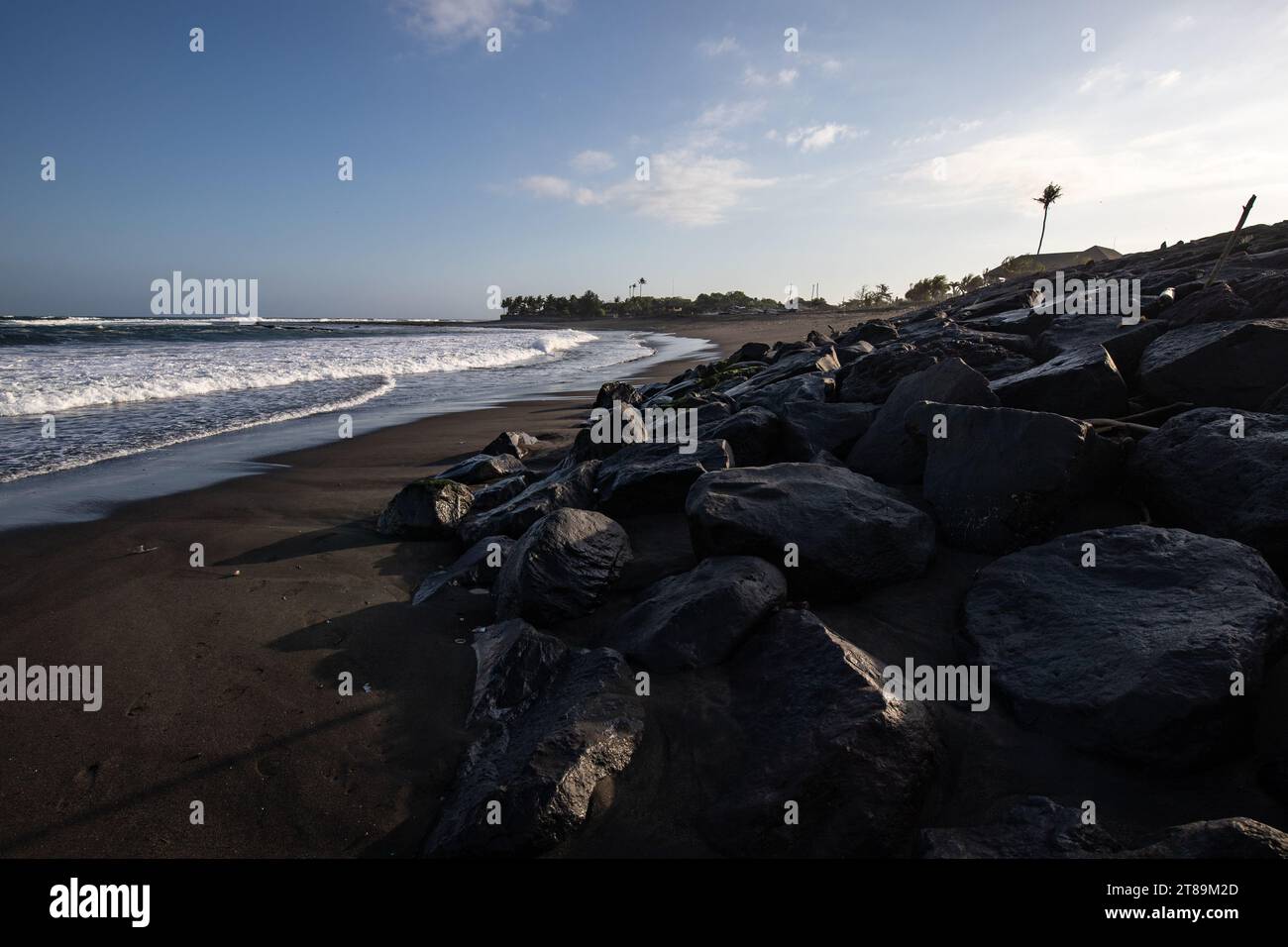 Hindu temple on a black sand beach directly by the sea. Evening landscape with waves on the sea on tropical island in Sanur, Bali, Indonesia Stock Photo