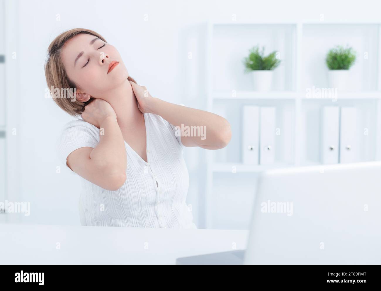 Young Asian woman suffering from neck pain in office Stock Photo