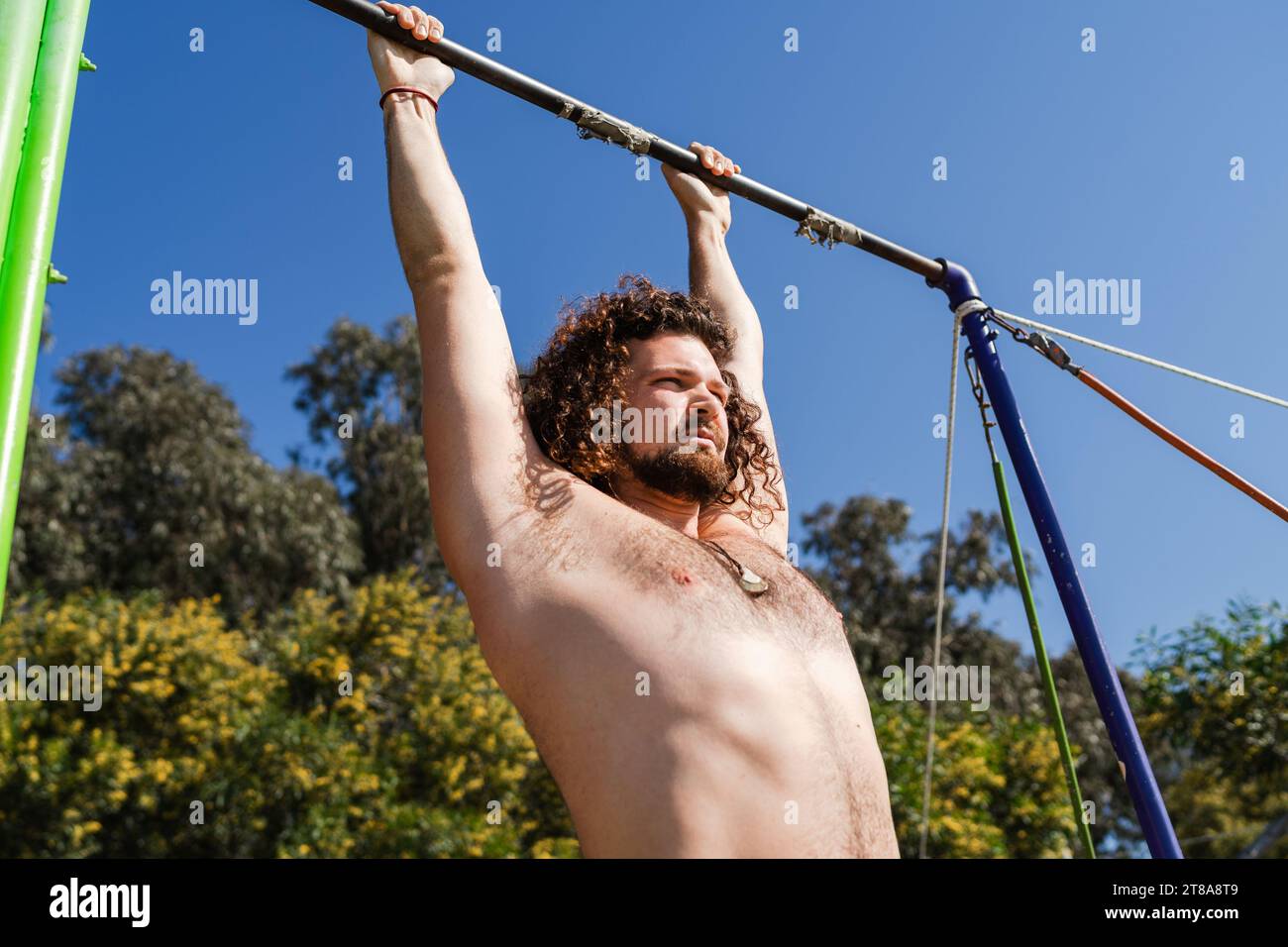 Curly and bearded man doing pull-ups on horizontal bar Stock Photo