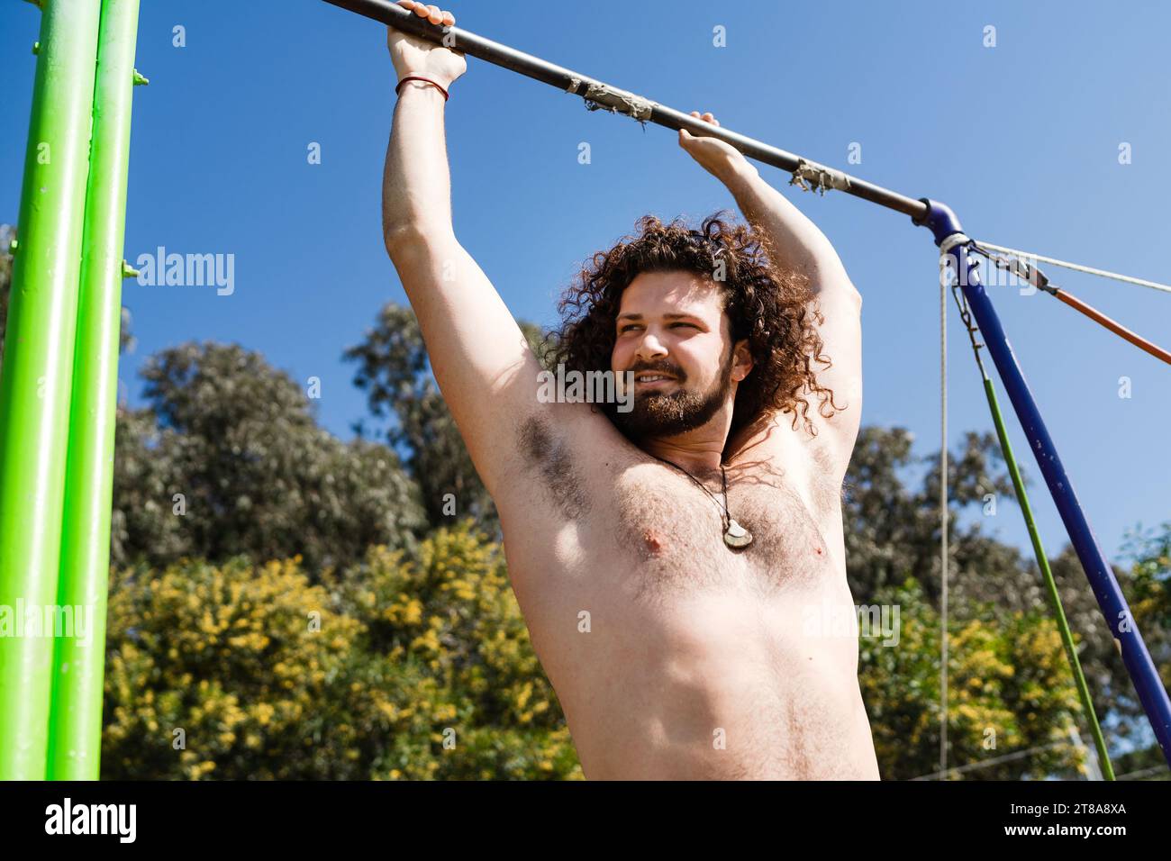 Curly and bearded man doing pull-ups on horizontal bar Stock Photo