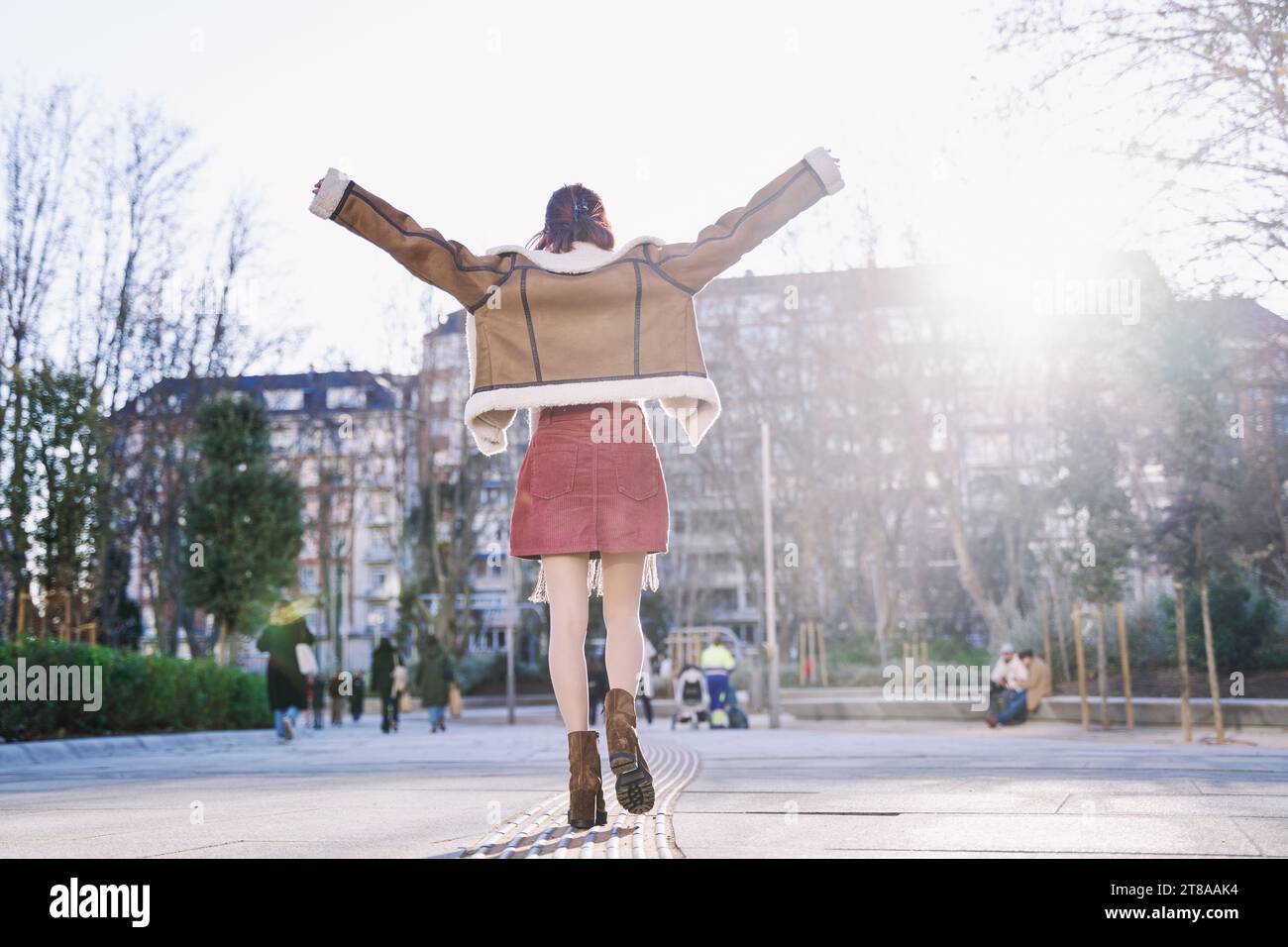 Happy young man with his back turned and hands up. woman in backlight walking in the city. Stock Photo