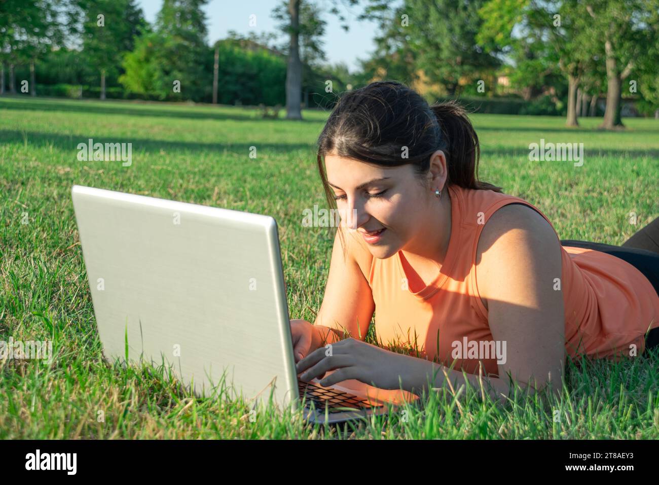 Young Caucasian woman lying on park using her laptop very happy Stock Photo