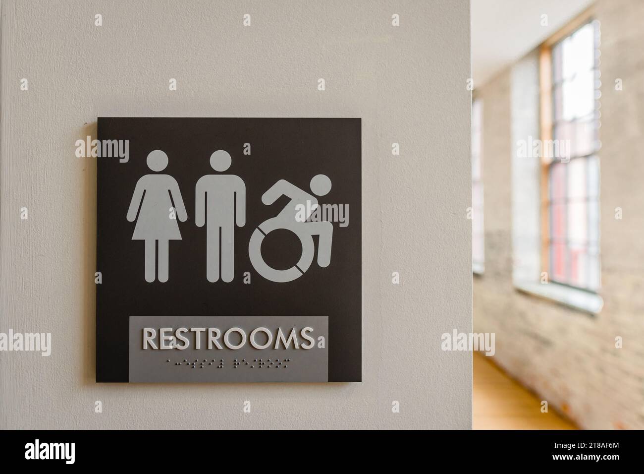 Close-up of unisex bathroom sign against neutral colored wall with symbols for male, female, and wheelchair. Copy space. Stock Photo