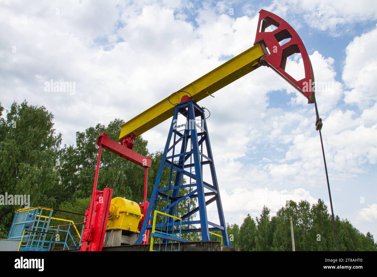 oil pumpjack for oil production against a cloudy sky stands among the trees Stock Photo
