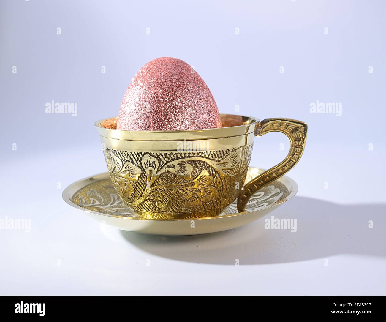 A Shimmering Pink Easter Egg in a Graceful Golden Teacup Stock Photo