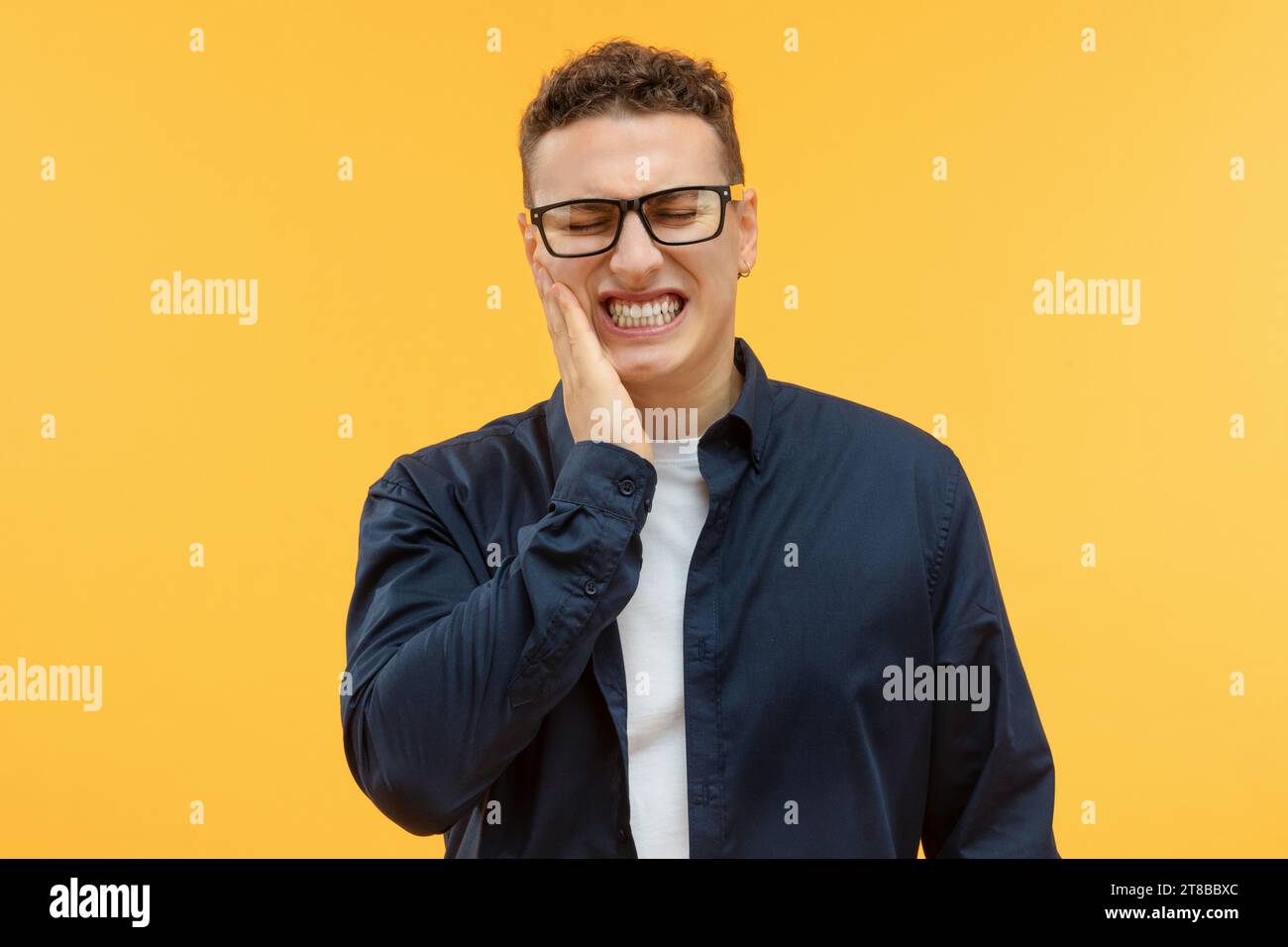 Unhappy young guy holding hand on cheek Stock Photo
