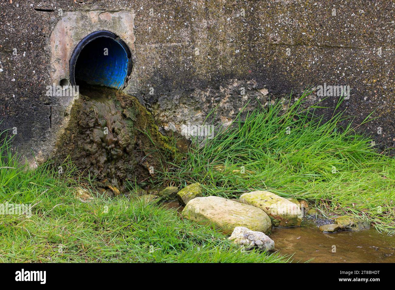 An outflow pipe with a large volume of waste flowing out of it onto the