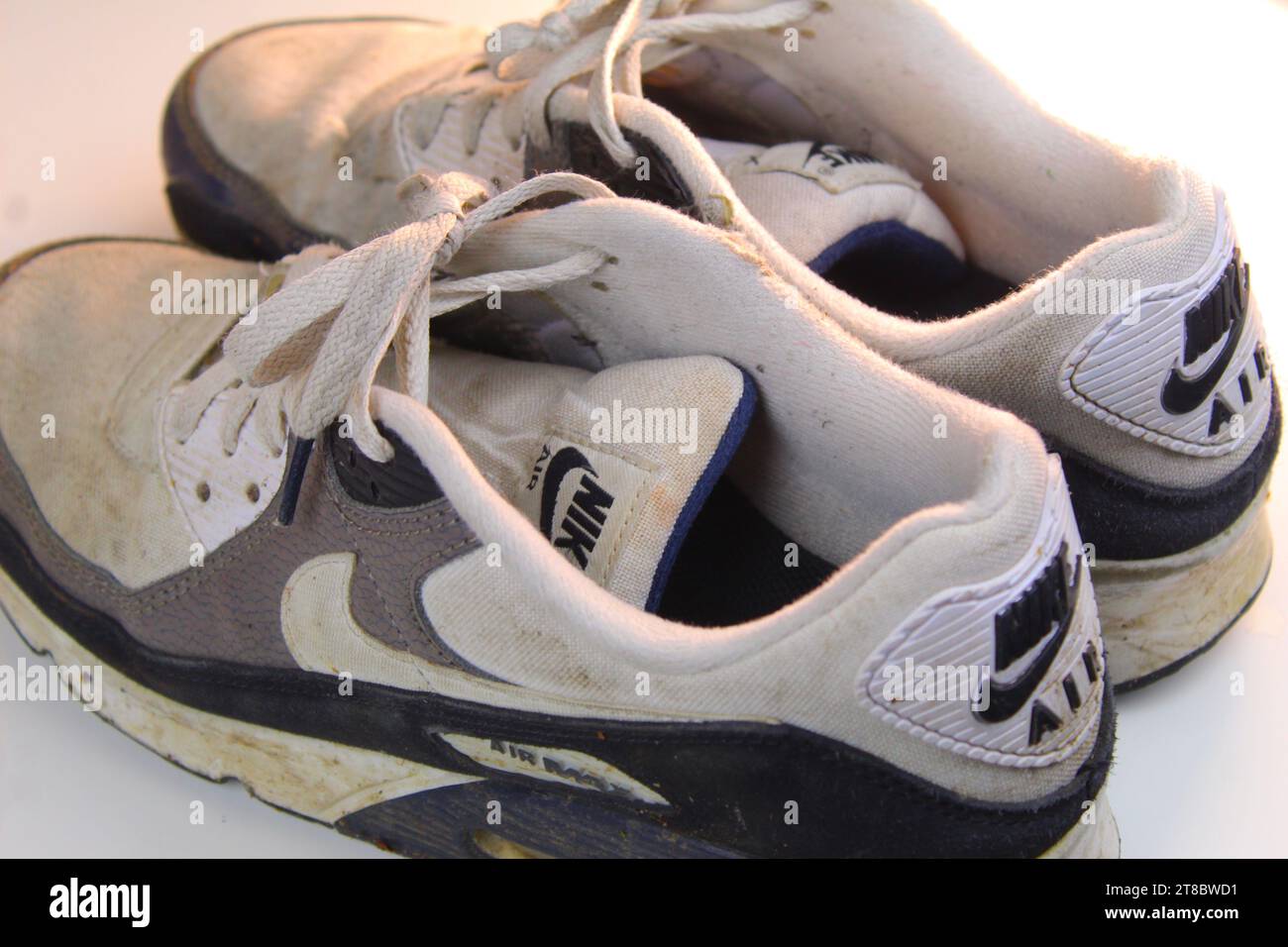 A photo of a pair of  dirty white Nike Air Max 90 runners on a white surface. Stock Photo