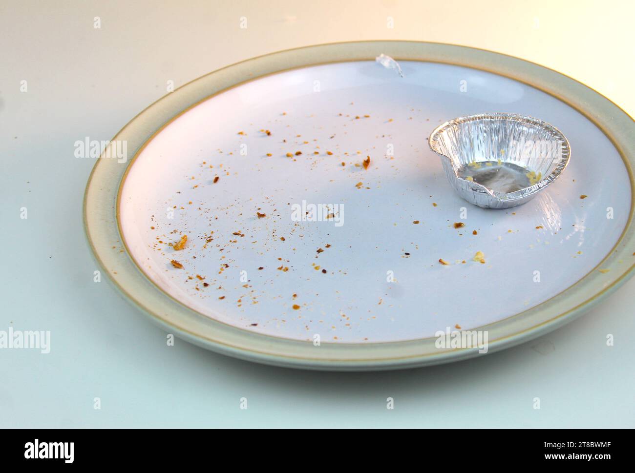 A photo of an empty silver mince pie tin on a white plate covered in crumbs on a white desk. Stock Photo