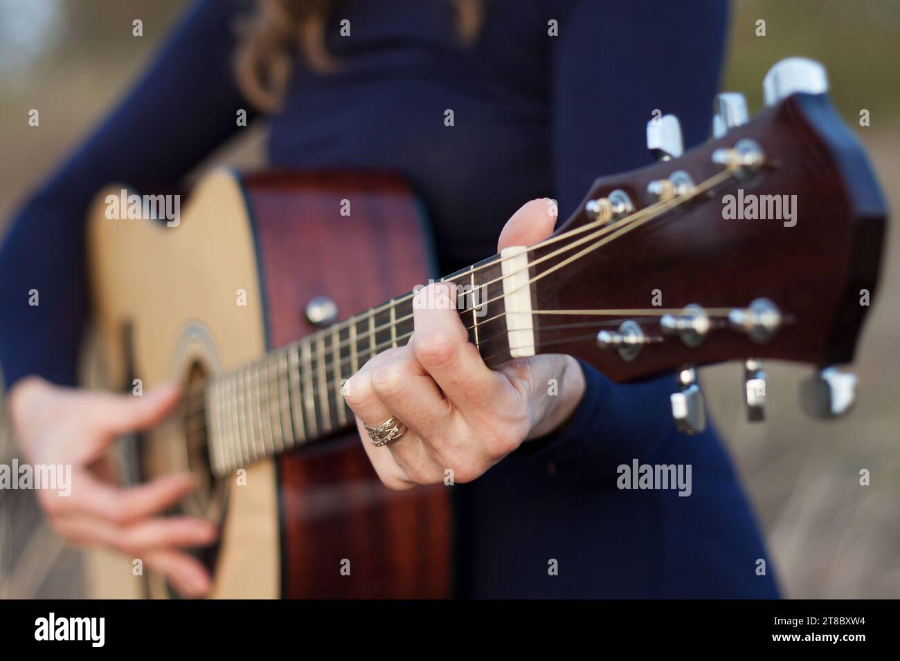 Close-up of woman's hands playing an acoustic guitar. Outdoor leisure, creative evening, warm autumn, sunset. Romantic mood. Selective Focus Stock Photo