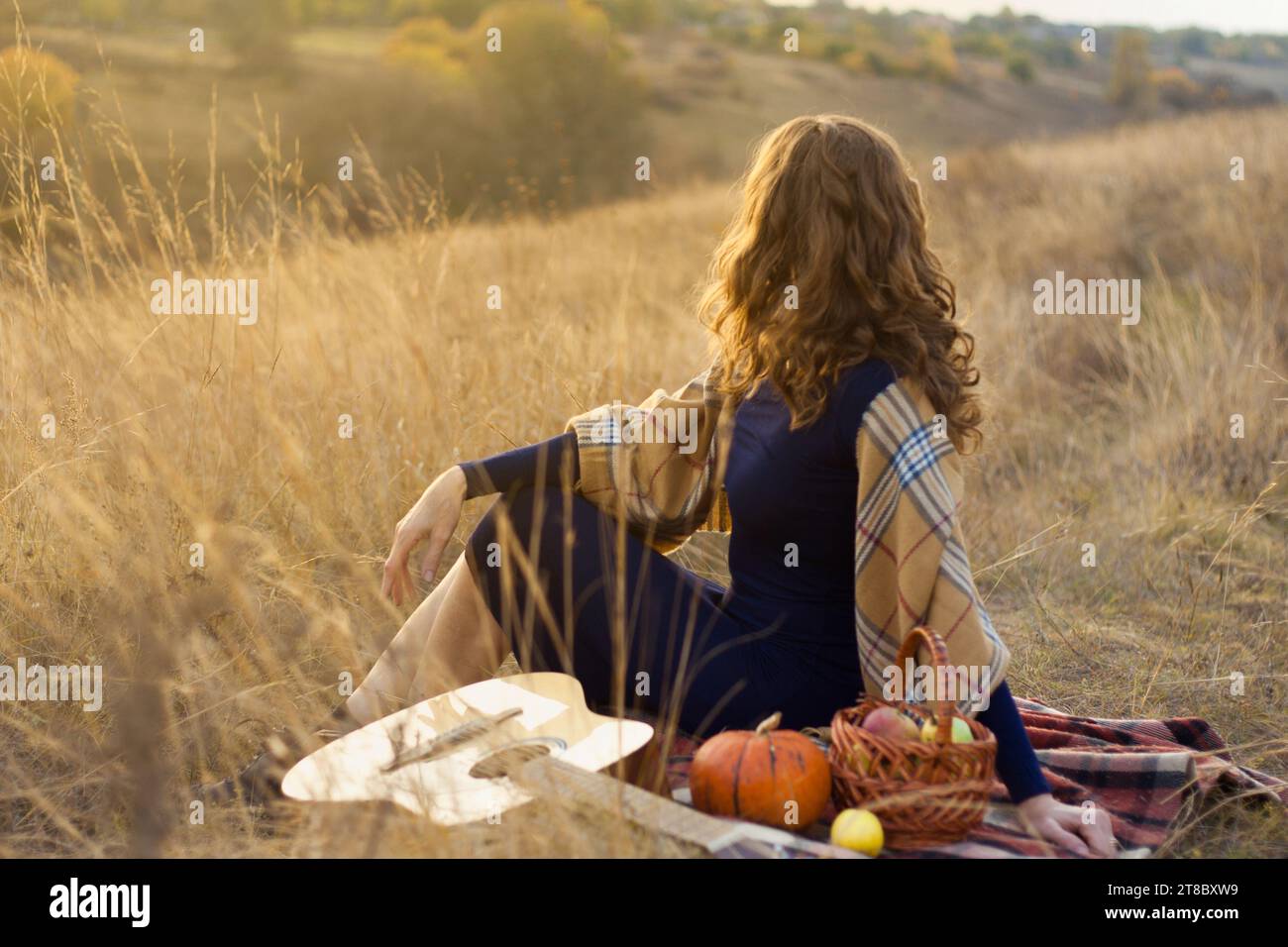 beautiful young woman musician finished playing melody on acoustic guitar and relaxing, sitting in field, enjoying autumn sunset. Outdoor Picnic. Roma Stock Photo