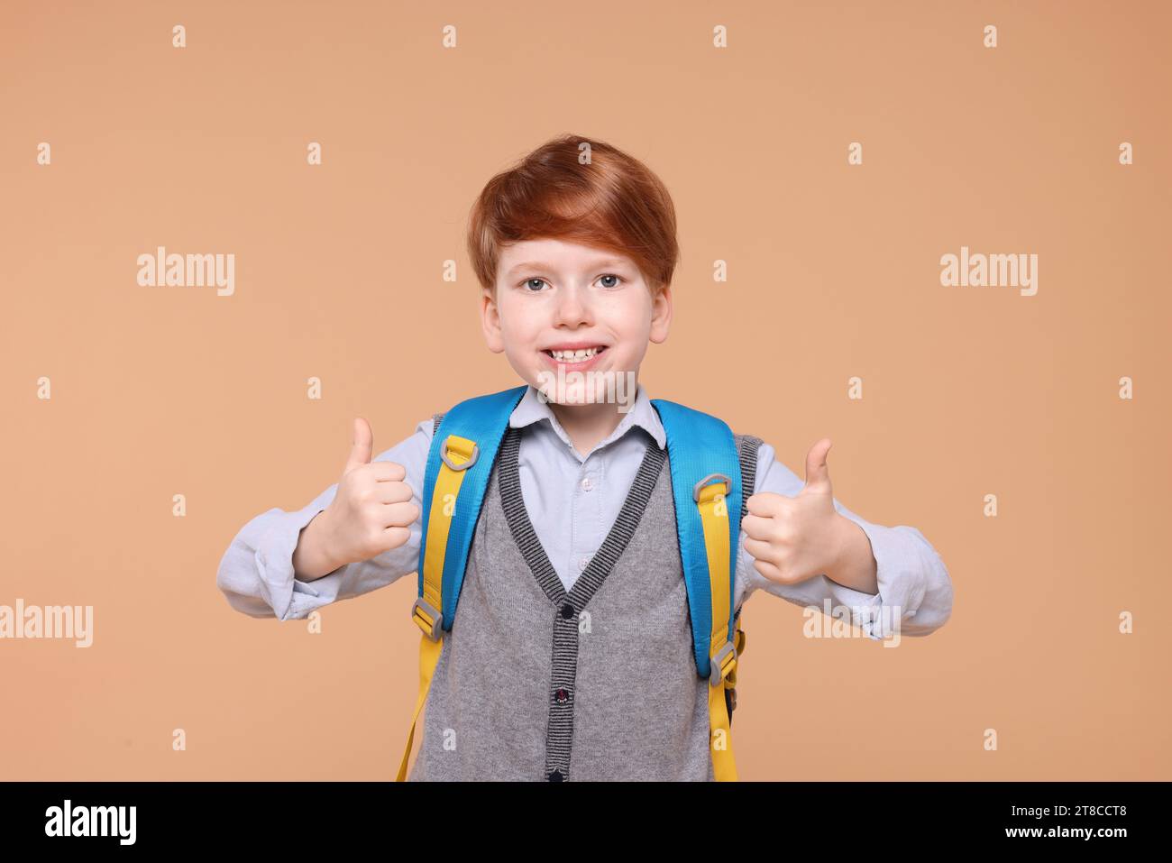 Smiling schoolboy showing thumbs up on beige background Stock Photo - Alamy