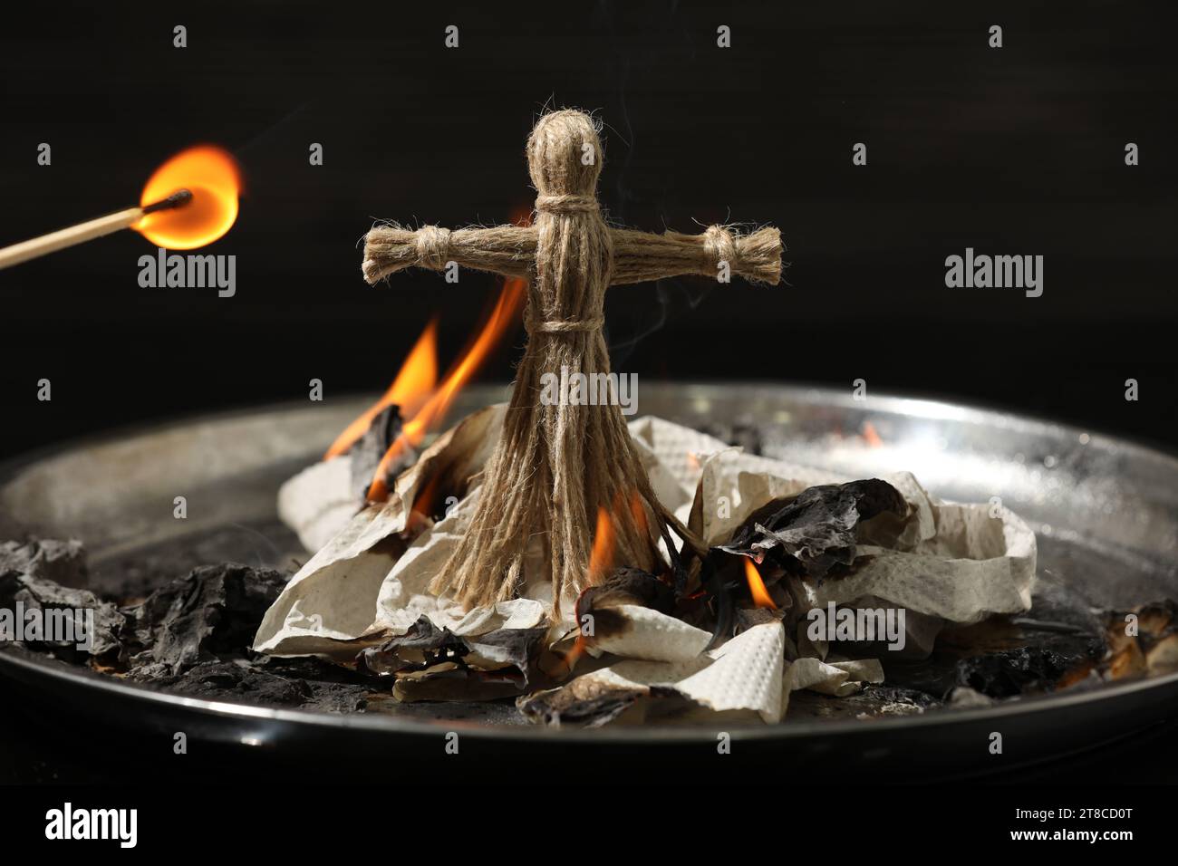 Voodoo doll burning in metal tray on dark background. Curse ceremony