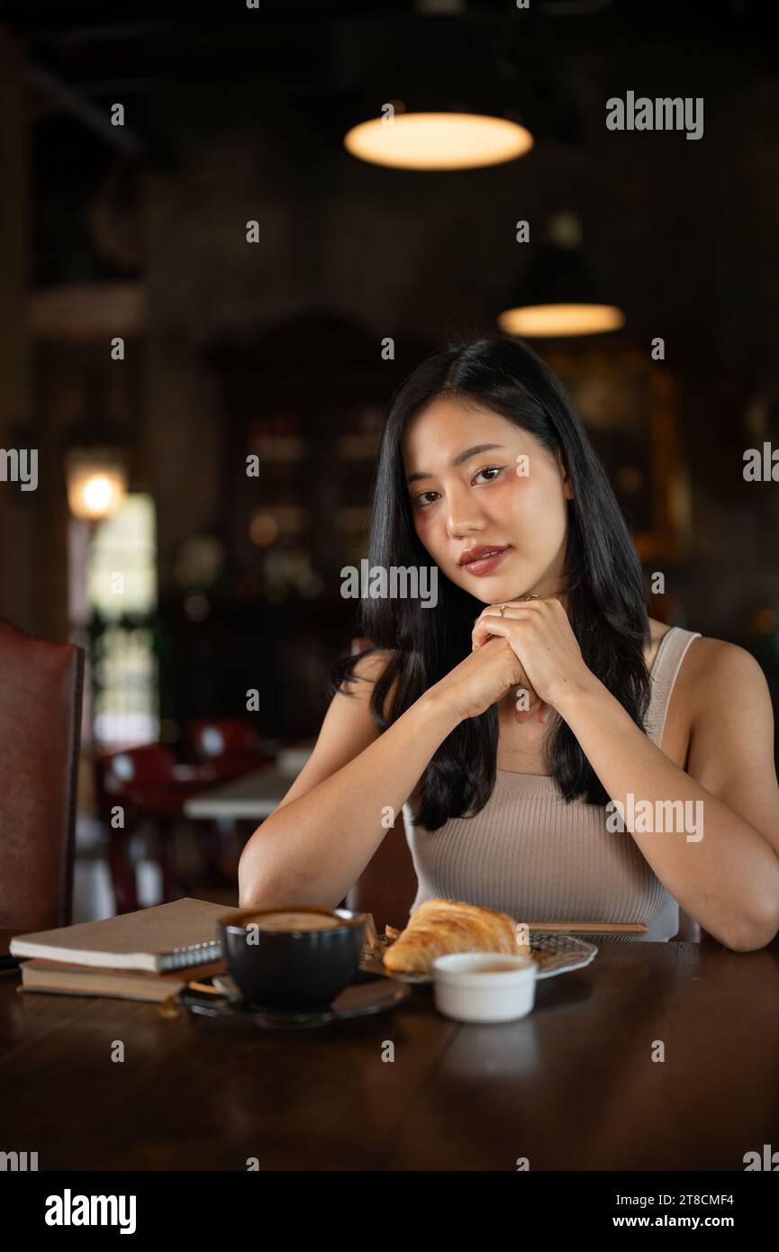Portrait of young elegant Asian woman looking at the camera while sitting in the dark vintage living room. Stock Photo