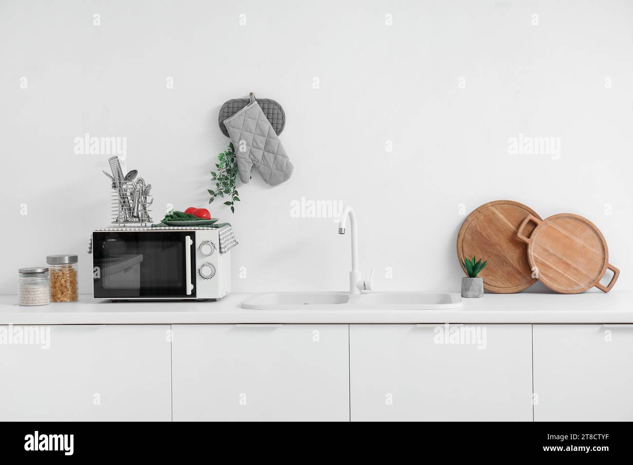 Interior of light kitchen with microwave oven, sink and utensils on white counters Stock Photo