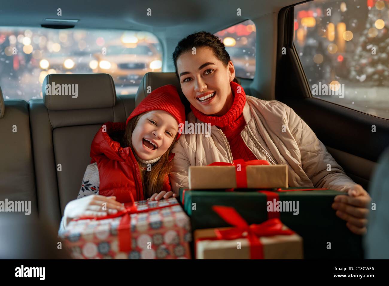 Woman and her child  holding presents and delivering them on car to home. Holidays concept. Time of Christmas Eve. Stock Photo