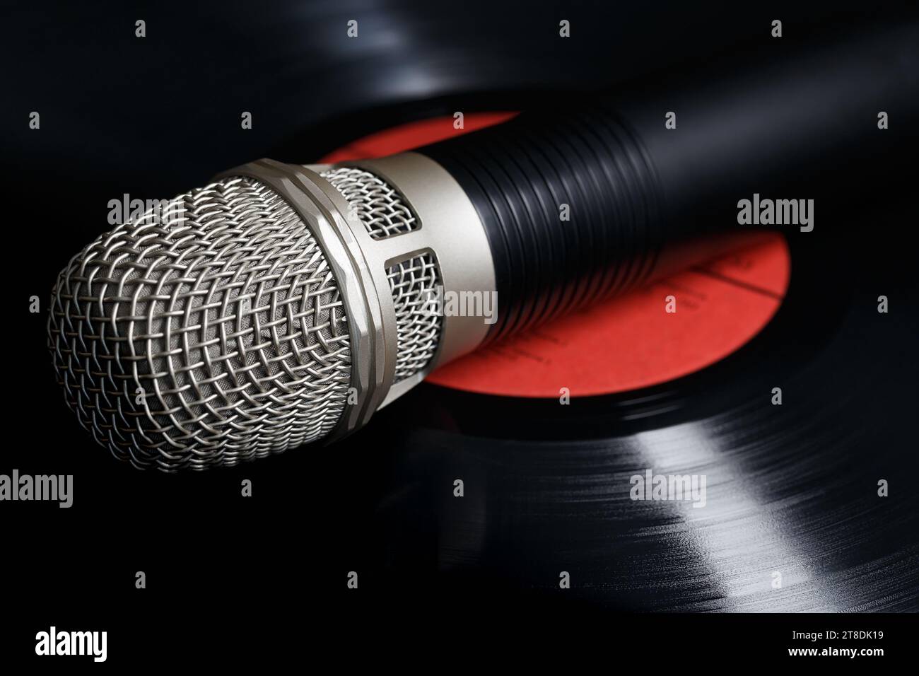 The microphone is lying on a vinyl record, with the reflection of light highlighting the sound tracks. Analogue sound recording concept Stock Photo