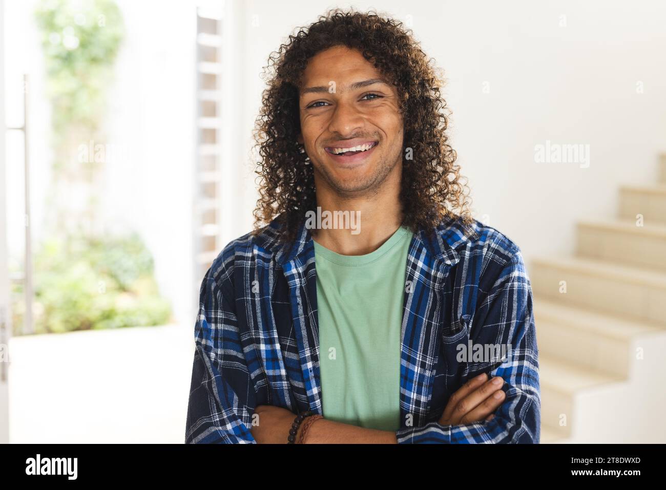 Happy biracial man with long dark curly hair laughing in sunny living room at home Stock Photo