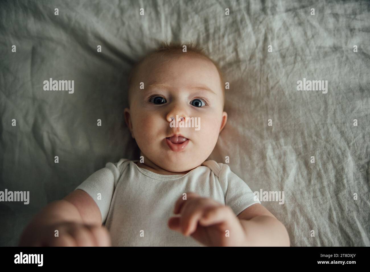 Overhead close up of baby laying on bed and sticking out tongue Stock Photo