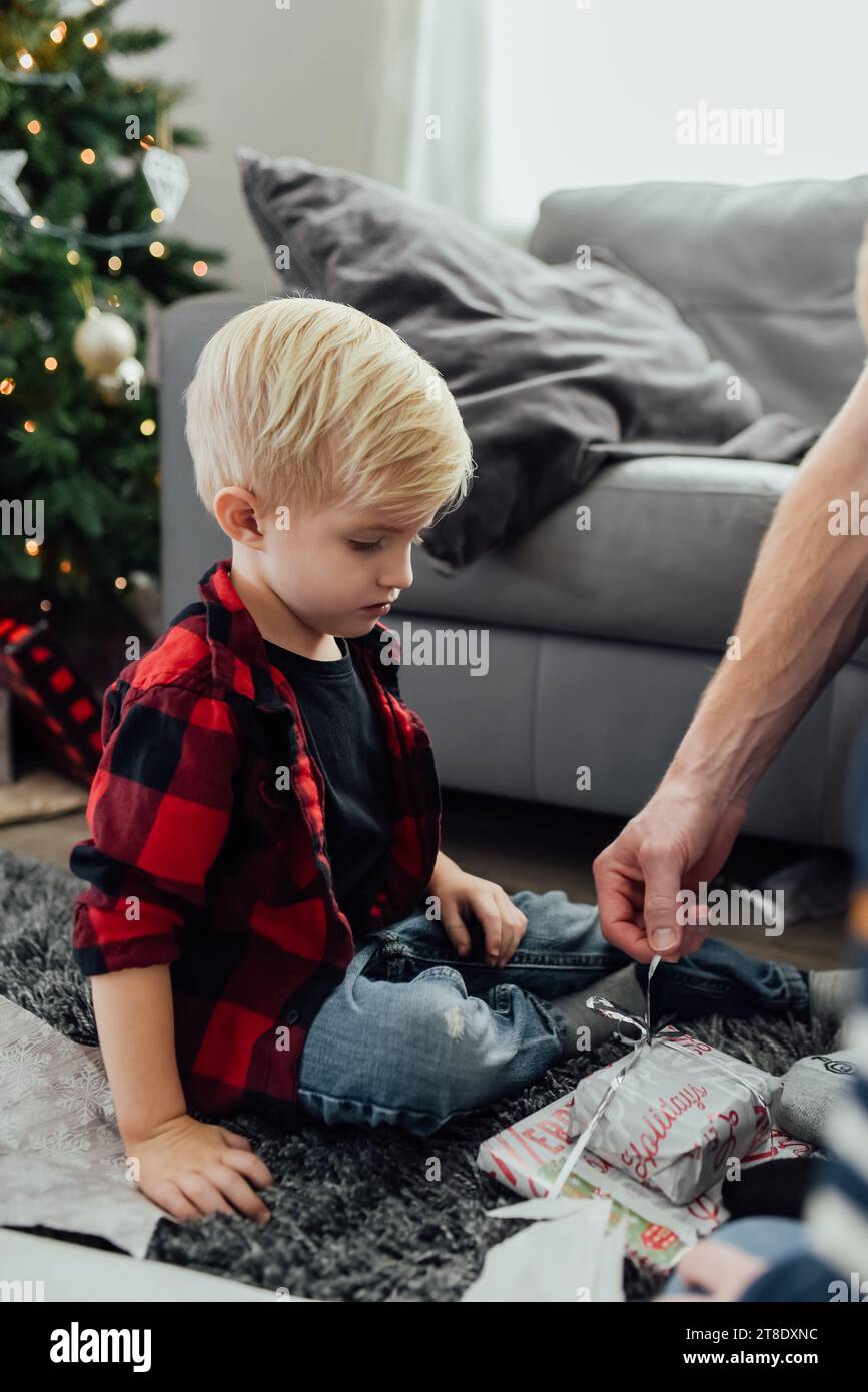 Little boy sits on floor in front of christmas tree at home whil Stock Photo