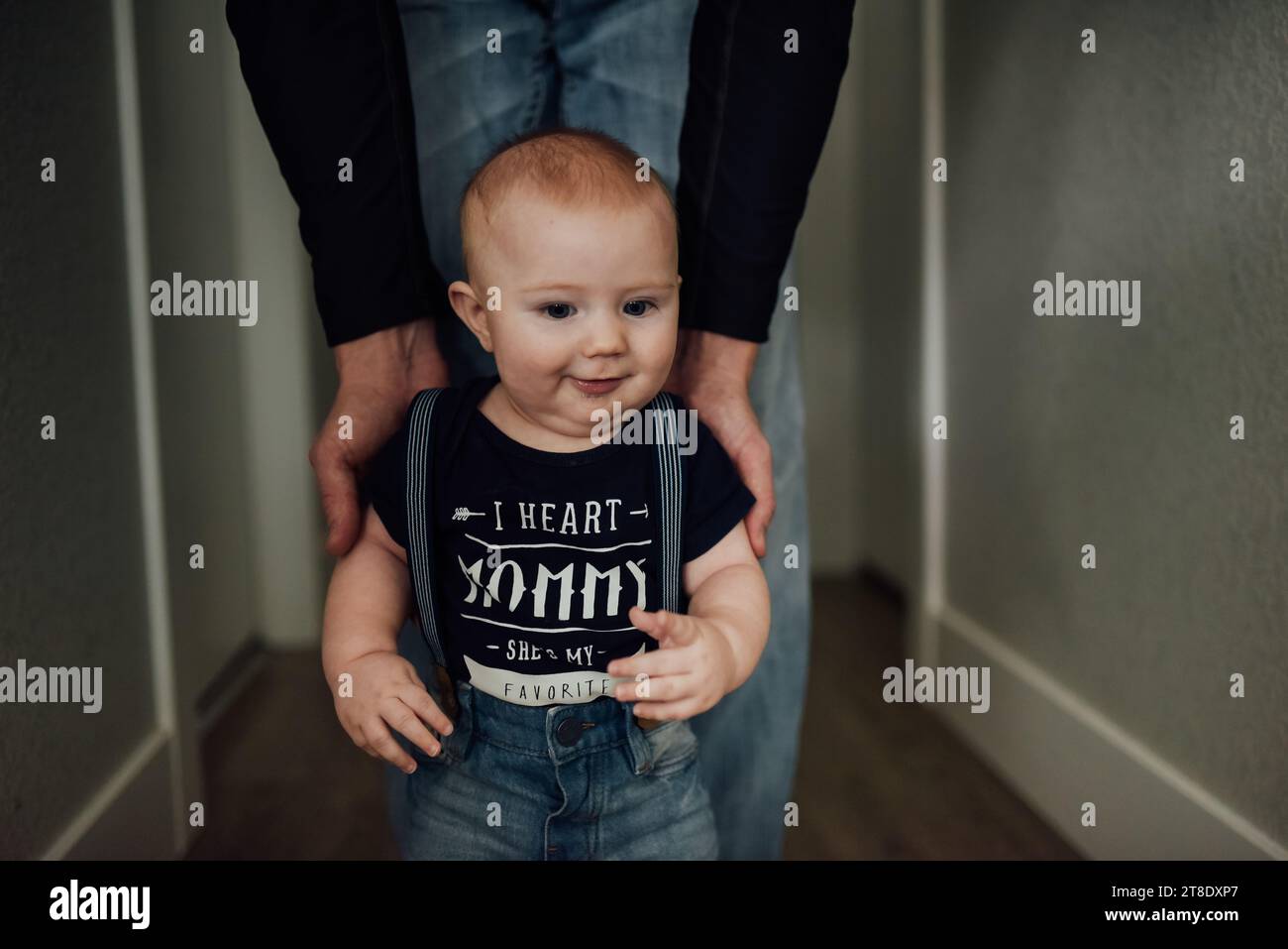 Dad helps baby boy stand in hallway at home. Stock Photo