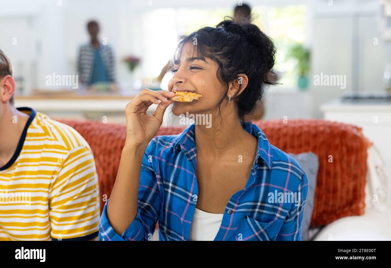 Happy diverse group of teenage friends sitting on couch and eating pizza Stock Photo