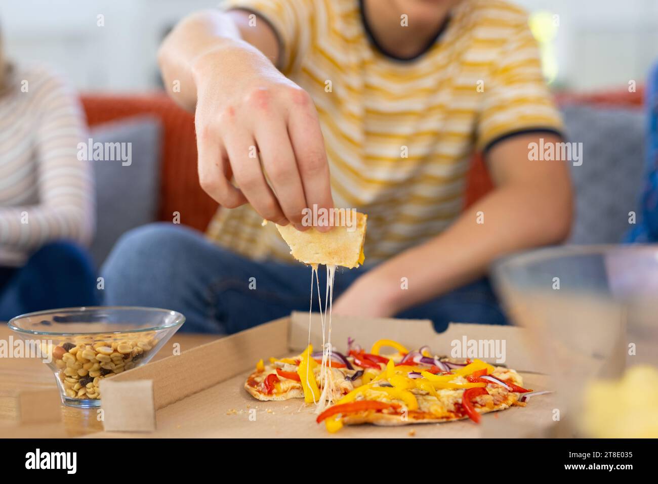 Diverse group of teenage friends sitting on couch and eating pizza Stock Photo