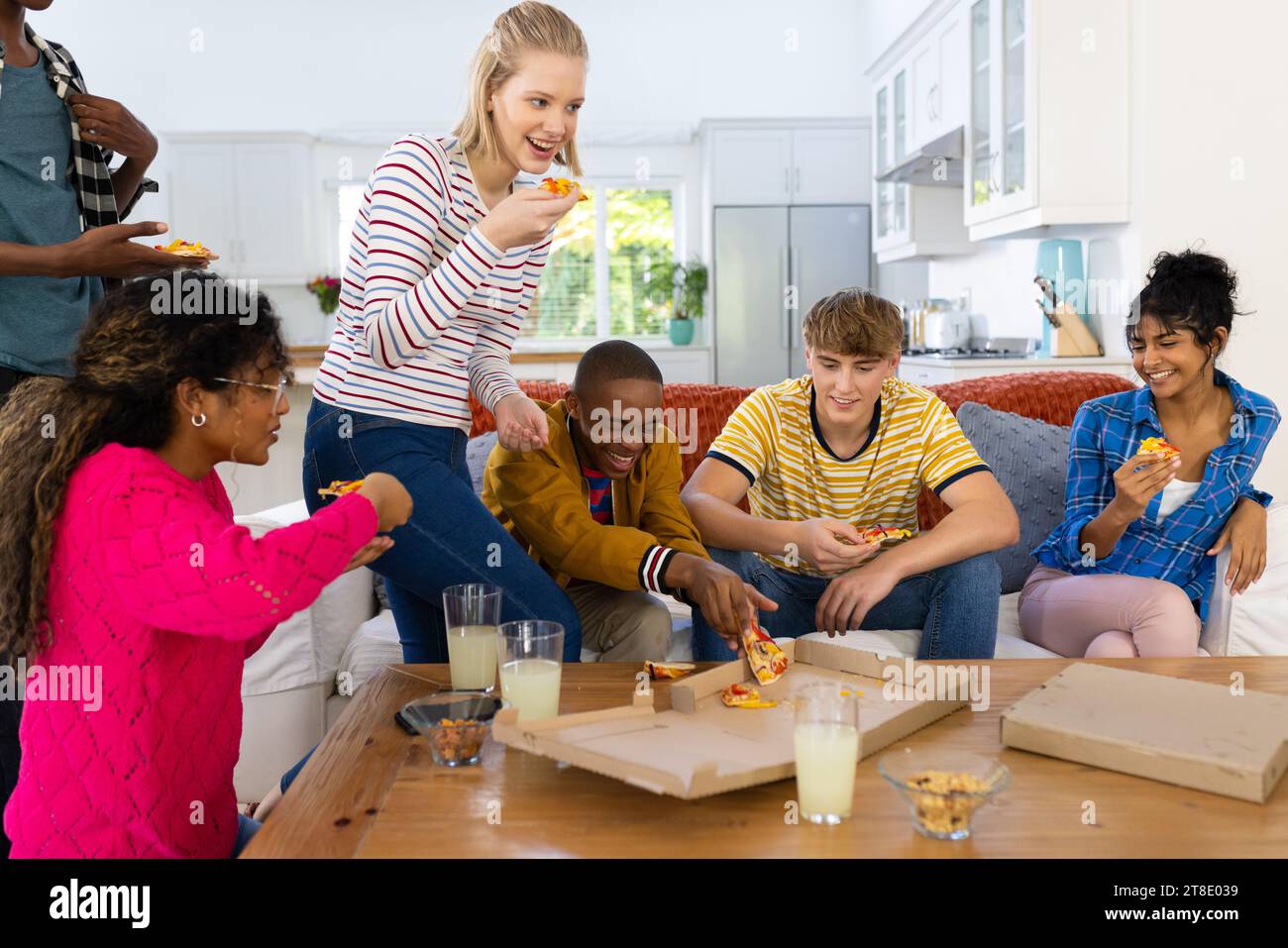 Happy diverse group of teenage friends sitting on couch and eating pizza Stock Photo