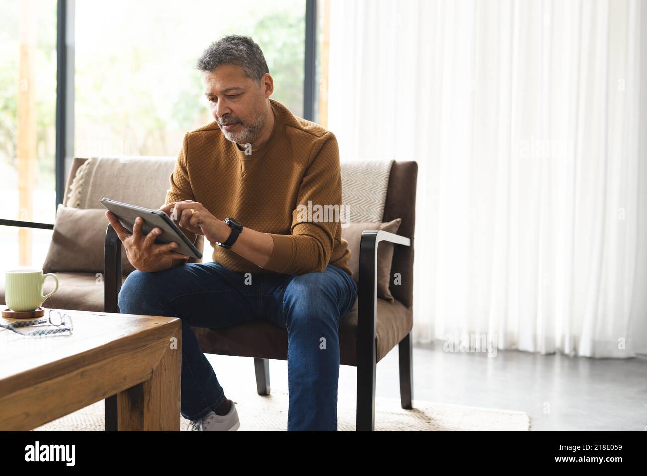 Senior biracial man sitting in armchair and using tablet at home Stock Photo
