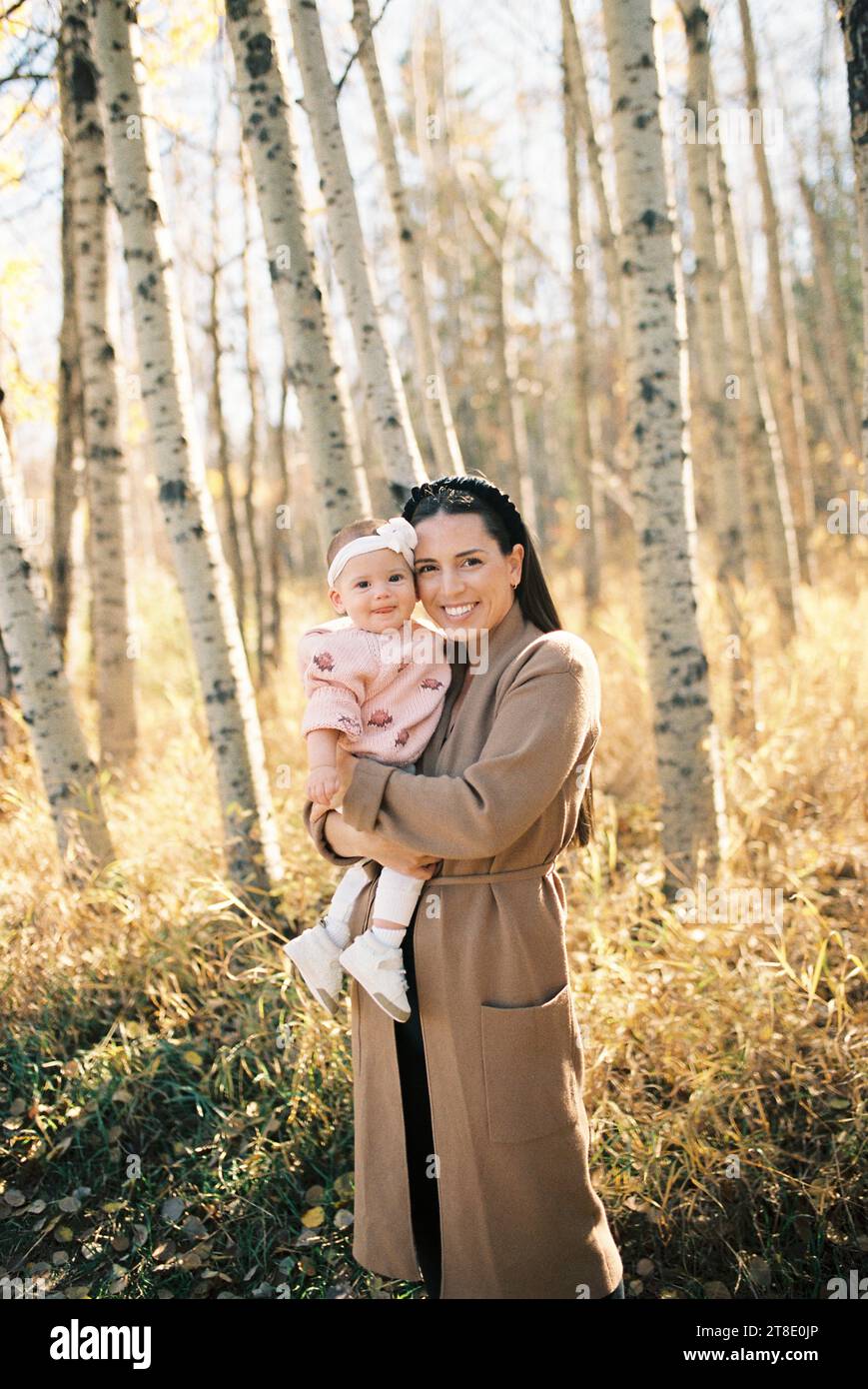 Mom holding smiling baby girl in yellow fall leaves and autumn forest Stock Photo