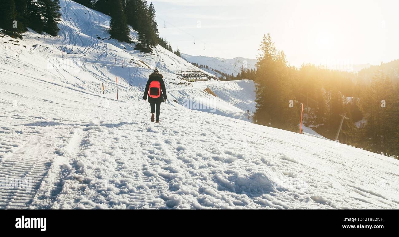 Young woman walking on snow mountain track during winter time at sunset - Travel and landscape nature concept - Focus on body Stock Photo