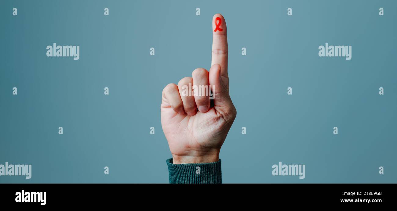 the hand of a man with a red awareness ribbon, for the fight against AIDS, painted in his forefinger, against a gray background with some blank space Stock Photo