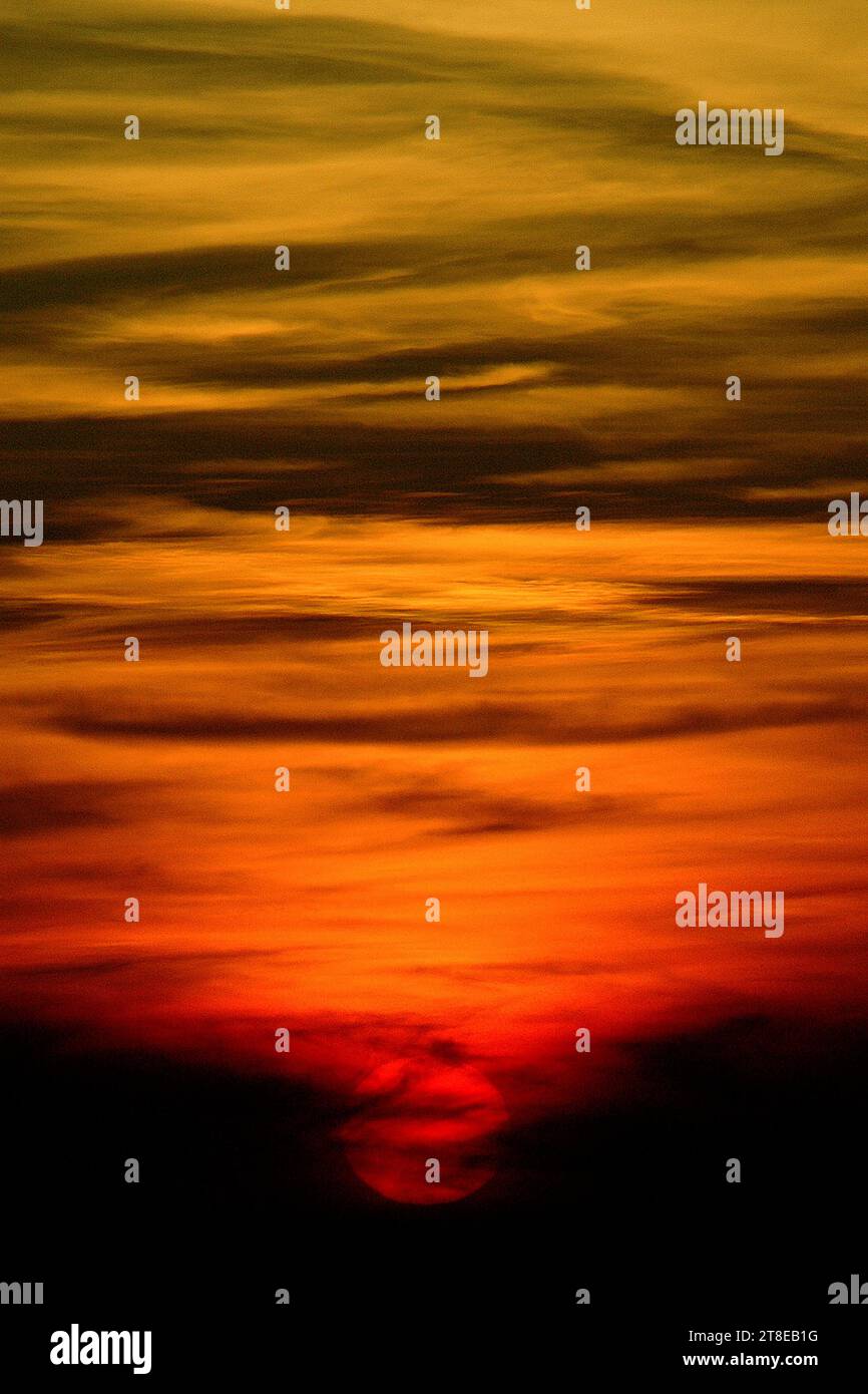 A red setting sun descends through a spiral of yellow, orange and black clouds at twilight. Stock Photo