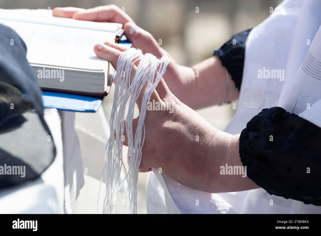 A hand gathers and holds the tzitzit, strings tied to the four corners