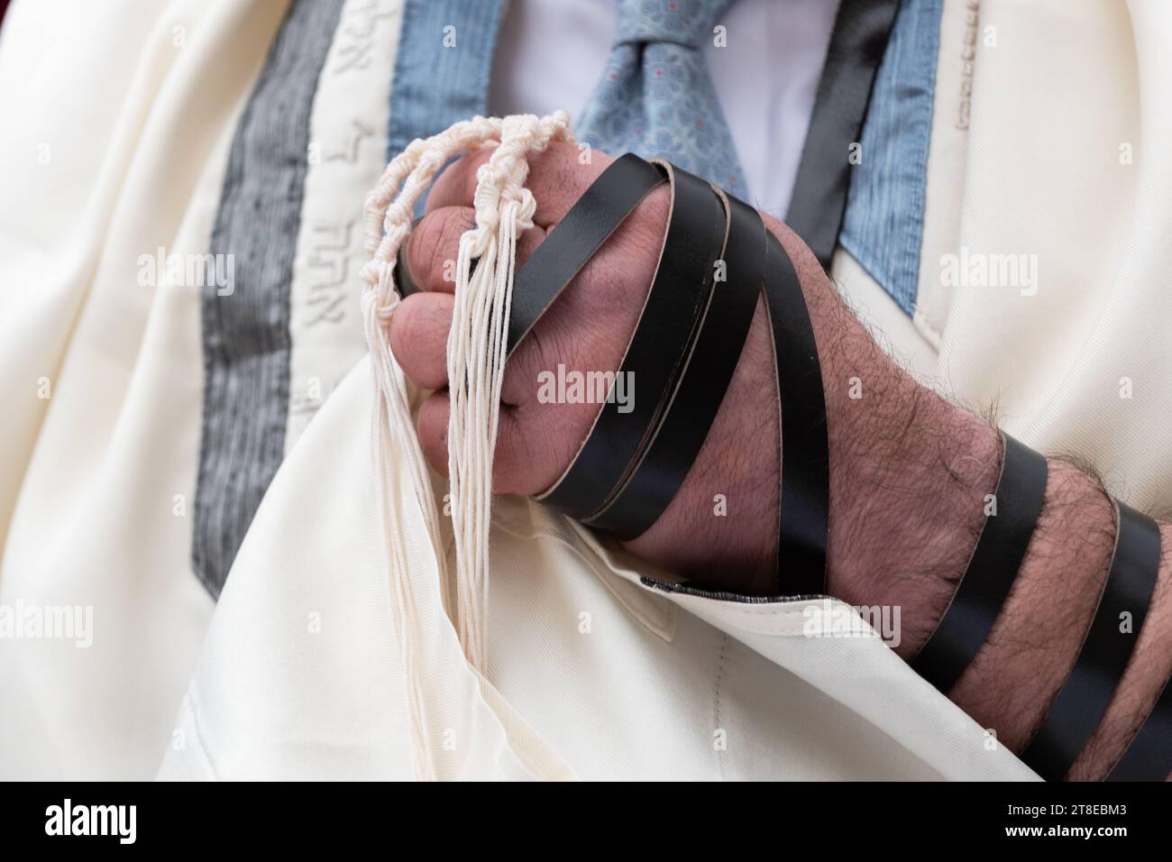 A hand gathers and holds the tzitzit, strings tied to the four corners