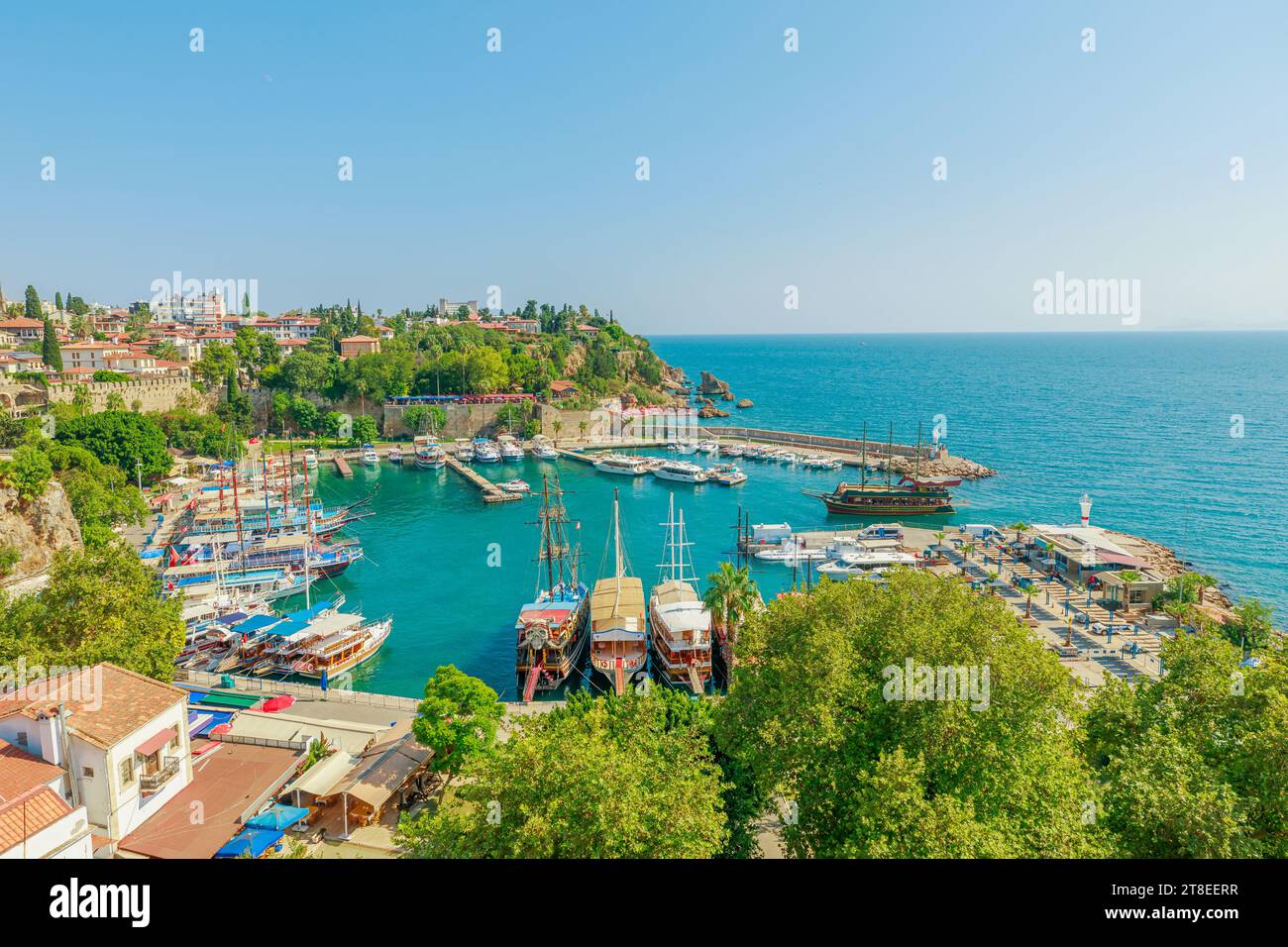 Panoramic view of Antalya, Turkey. Deep blue-green waters of the Mediterranean Sea meet a bustling harbor filled with boats of various sizes. A white Stock Photo
