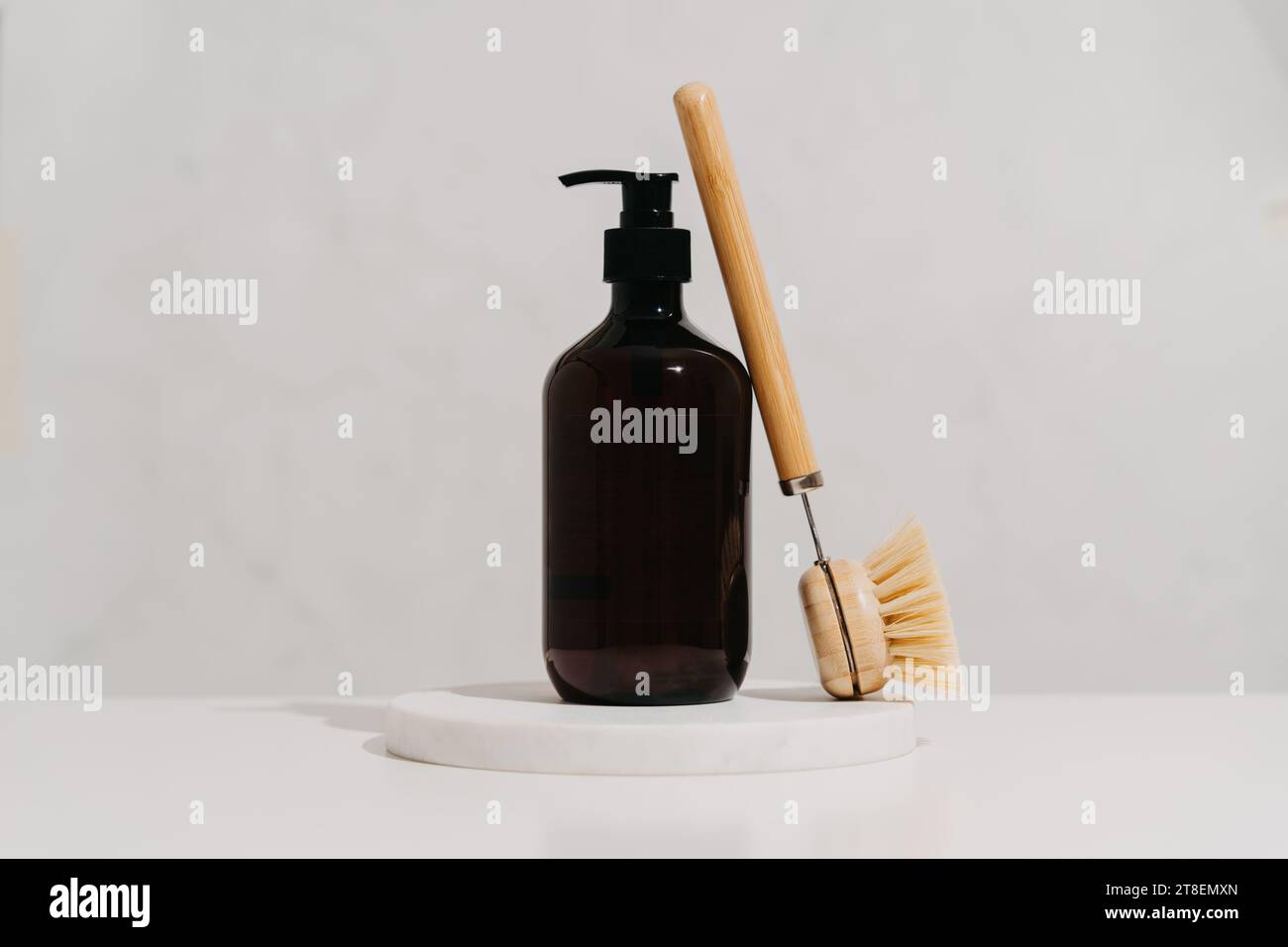 Amber bottle and wooden brush on marble shelf. Various items and ingredients for eco home cleaning. Front view. Copy space Stock Photo