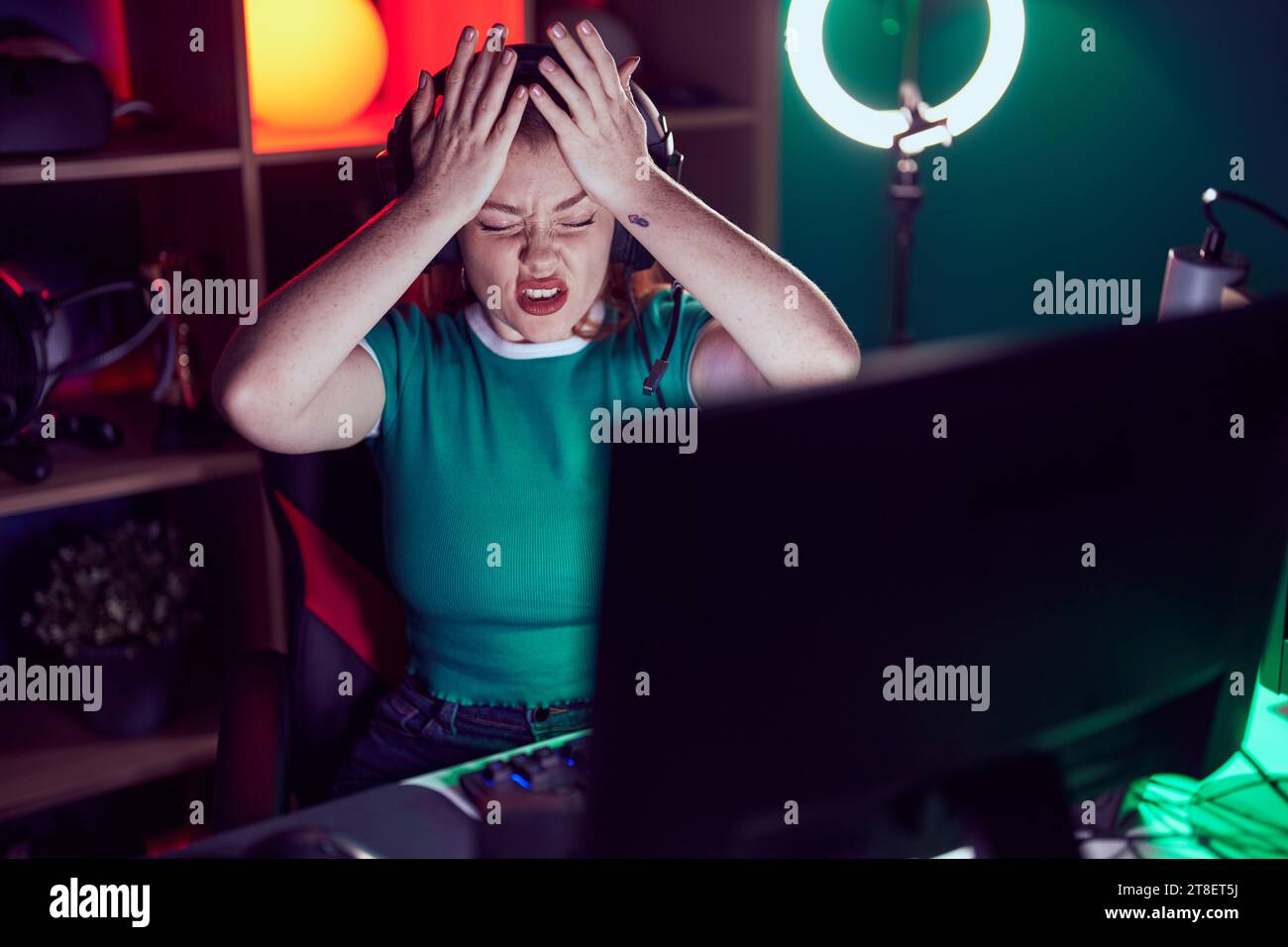 Redhead woman playing video games suffering from headache desperate and
