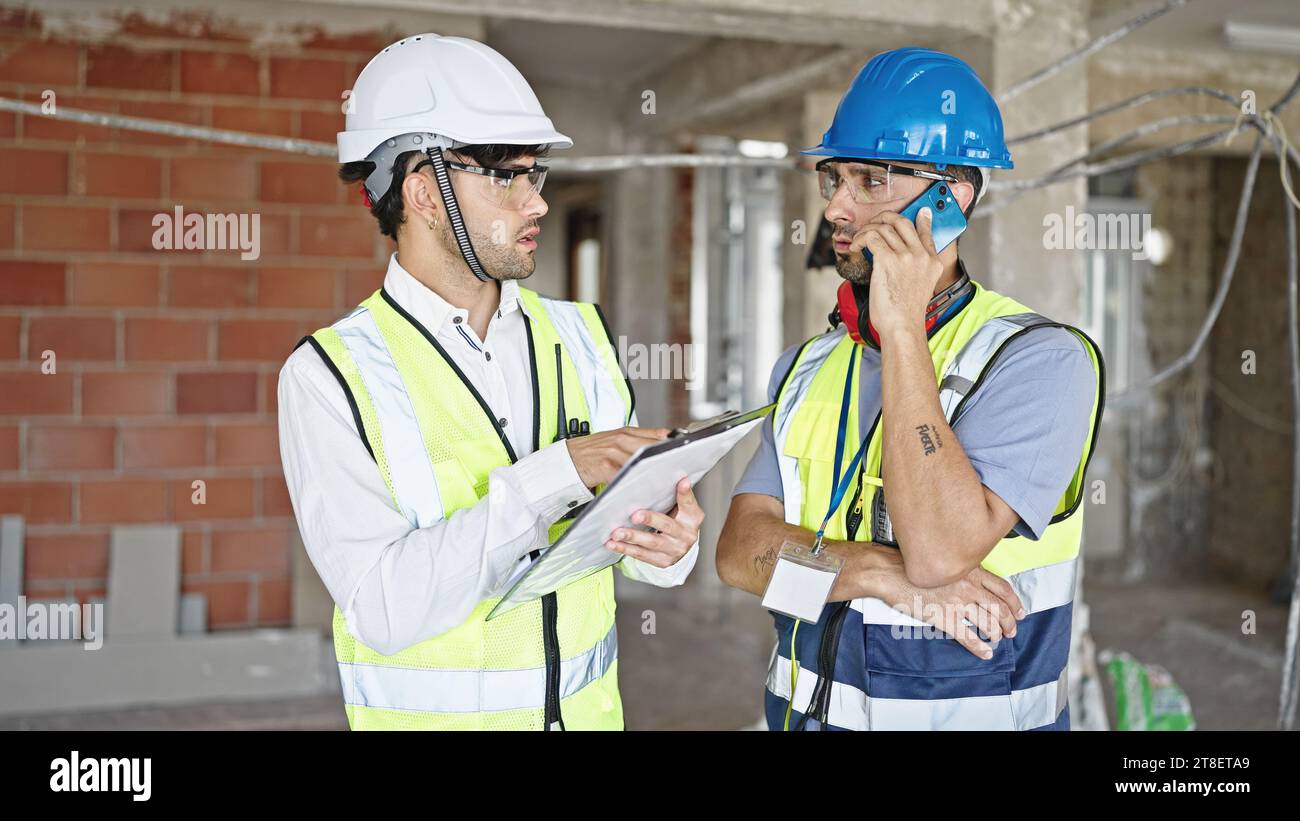 Two men builders talking on smartphone reading document at construction site Stock Photo