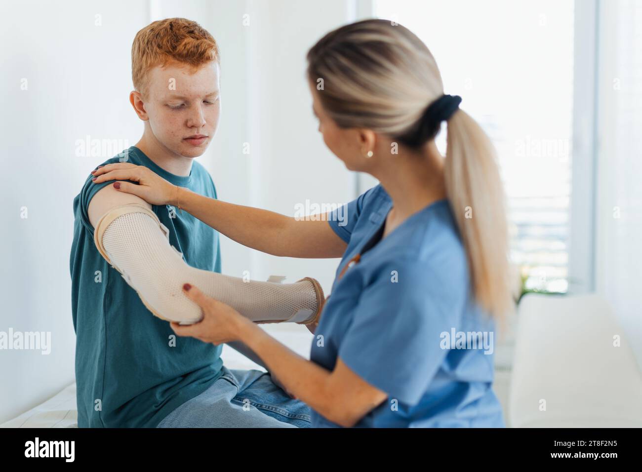 Doctor checking the orthopedic cast, brace on a teenage patient's broken arm. Teenage boy is healing a fracture after an accident. Stock Photo