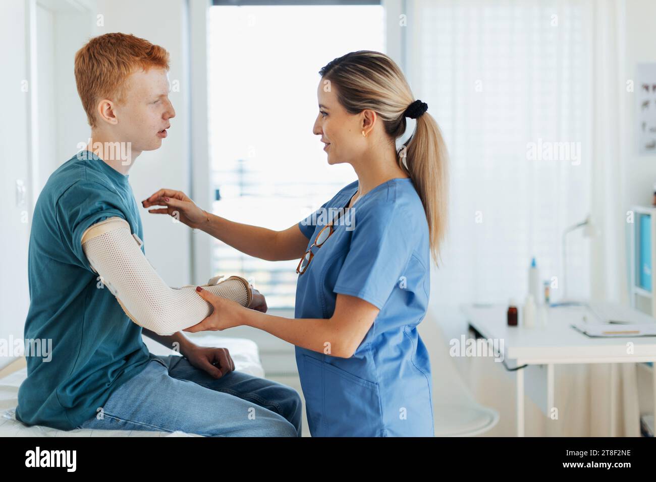 Doctor checking the orthopedic cast, brace on a teenage patient's broken arm. Teenage boy is healing a fracture after an accident. Stock Photo