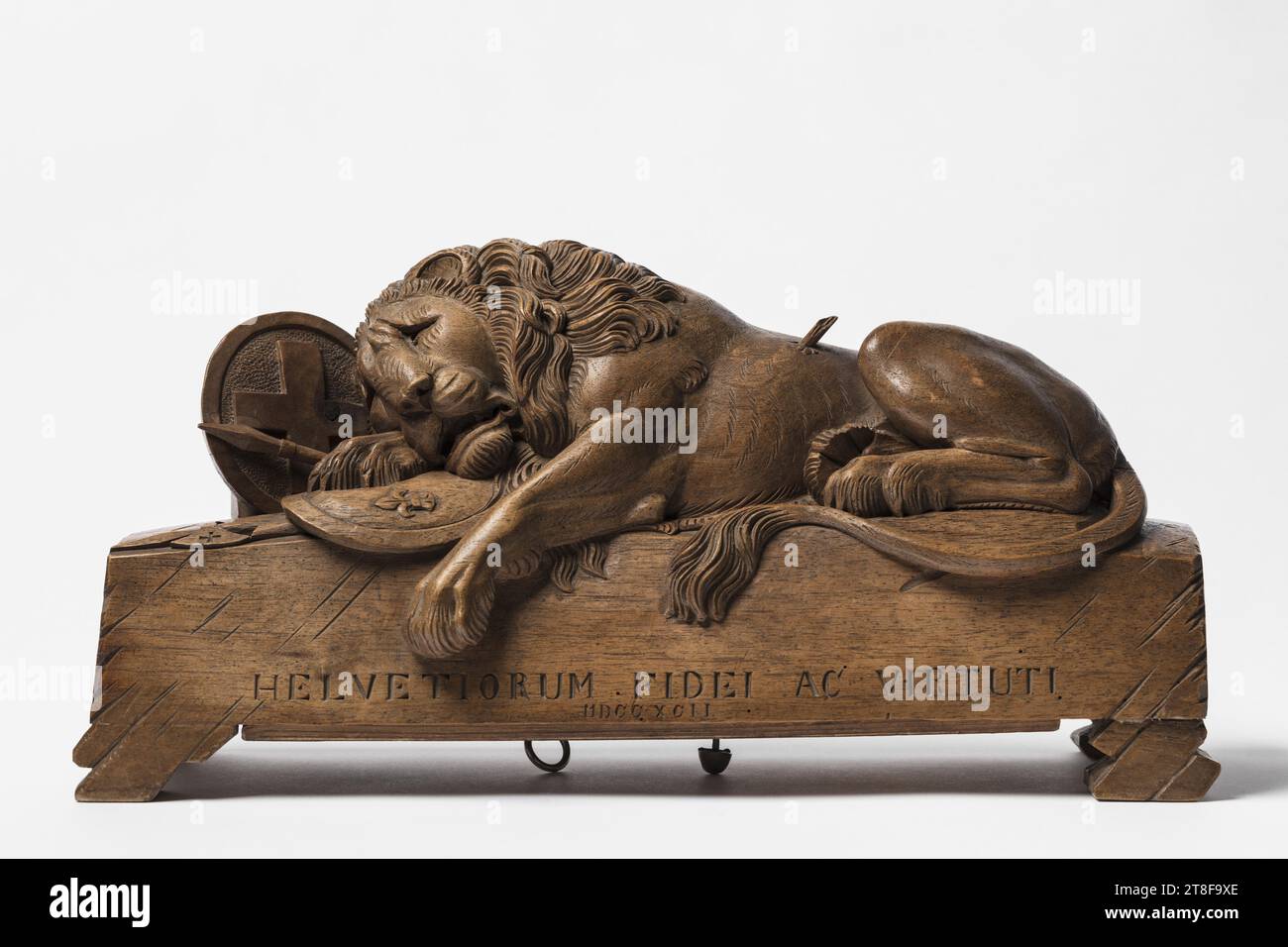 Dying Lion (The Lucerne Lion) with a Music Box, 1892, Musical Instrument, Music box, Sculpture, The dying lion, lying pierced by a spear, with its head and paw resting on the French coat of arms, is a smaller replica in Swiss walnut wood after Bertel Thorvaldsen's famous sandstone monument in Lucerne, 'Dying Lion (Swiss Lion)'. Swiss Lion Courage. Thorvaldsen's Swiss Lion was created in 1821, as a tribute to the Swiss Guardsmen who died during the Storming of the Tuileries on August 10, 1792, while defending the French King Louis XVI., Wood, Walnut, Metal, Carved, Height (maximum) 18 cm Stock Photo